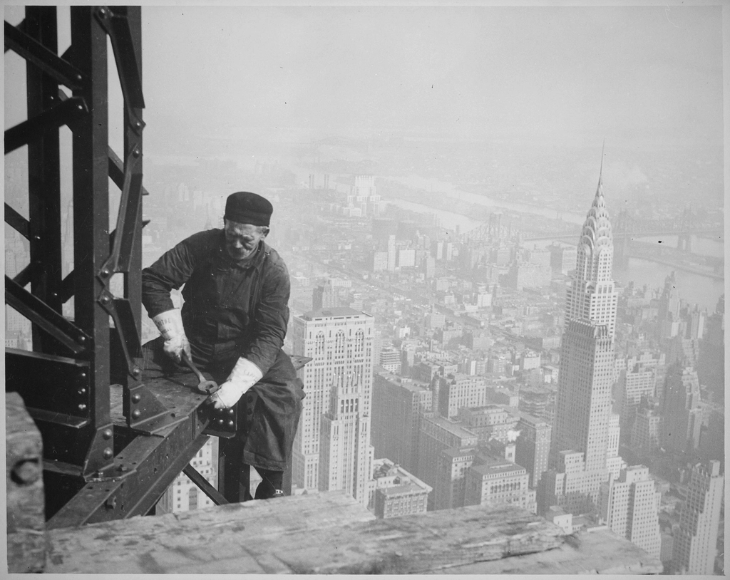 A worker bolting steel beams high on the Empire State Building, with Manhattan below